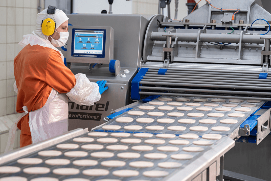 Colaborador com equipamento de proteção a supervisionar linha de produção alimentar industrial.