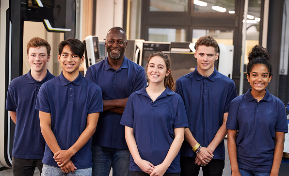 Grupo de seis profissionais com uniforme azul a posar juntos num ambiente industrial.