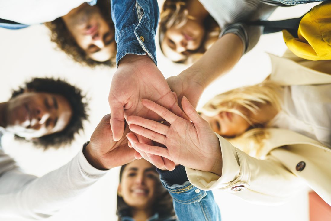 Grupo de pessoas a unir as mãos ao centro, simbolizando trabalho em equipe e espírito colaborativo.